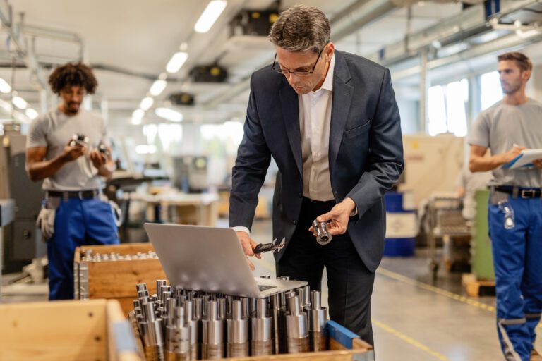 Mid adult engineer using laptop while performing quality control in steel factory